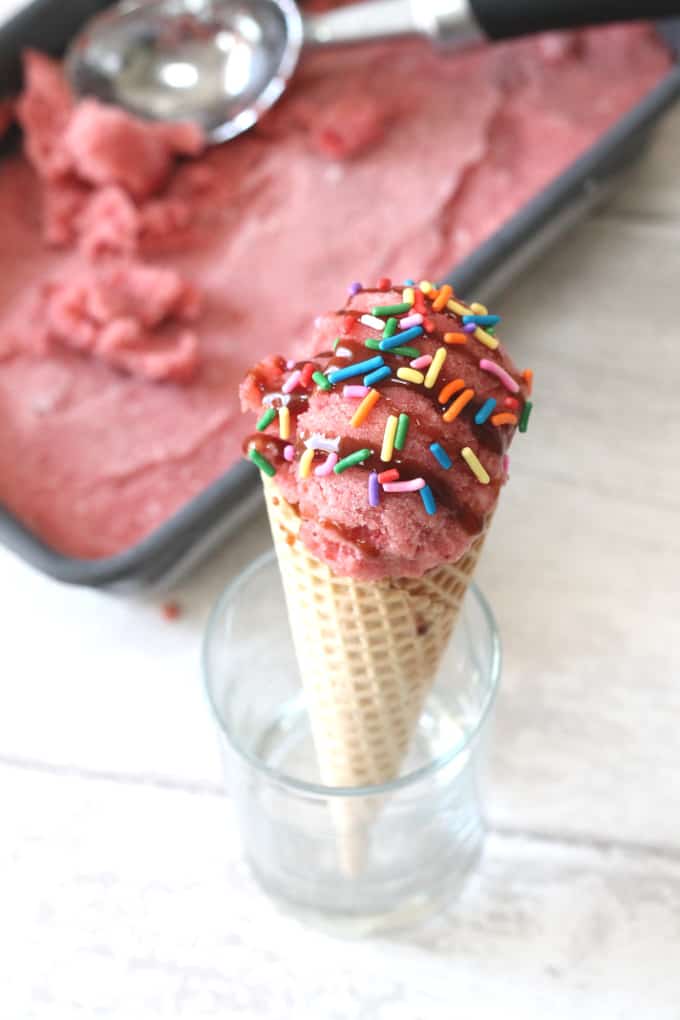 Two Ingredient Healthy Strawberry Ice Cream served in an ice cream cone and decorated with multi coloured sprinkles.