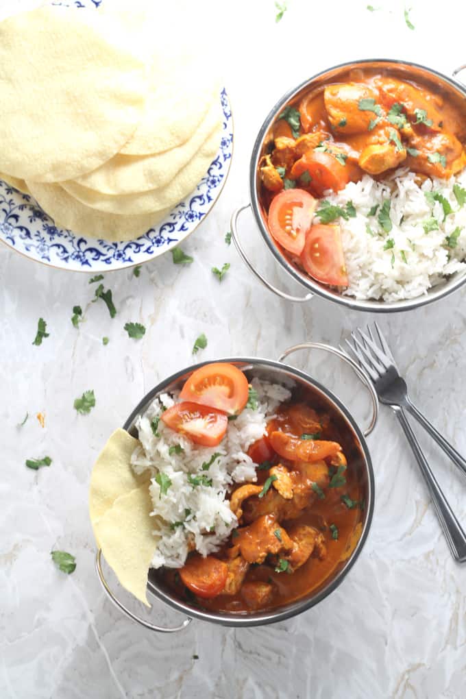 two bowls of the curry side by side with a knife and fork next to a plate of poppadoms