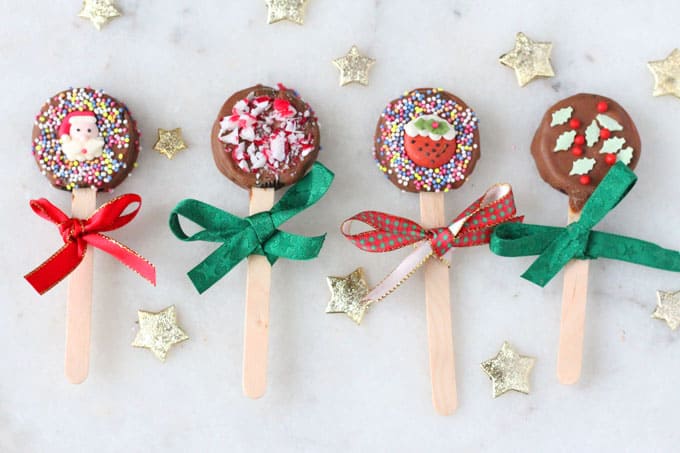 These festive Oreo Pops are coated in chocolate and decorated with Christmas sprinkles and icing decorations. They make a super cute edible gift that kids can make for their friends! dressed with red and green ribbons.