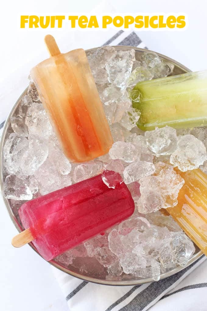 4 different coloured iced tea popsicles arranged on a bed of ice in a round stainless steel bowl.