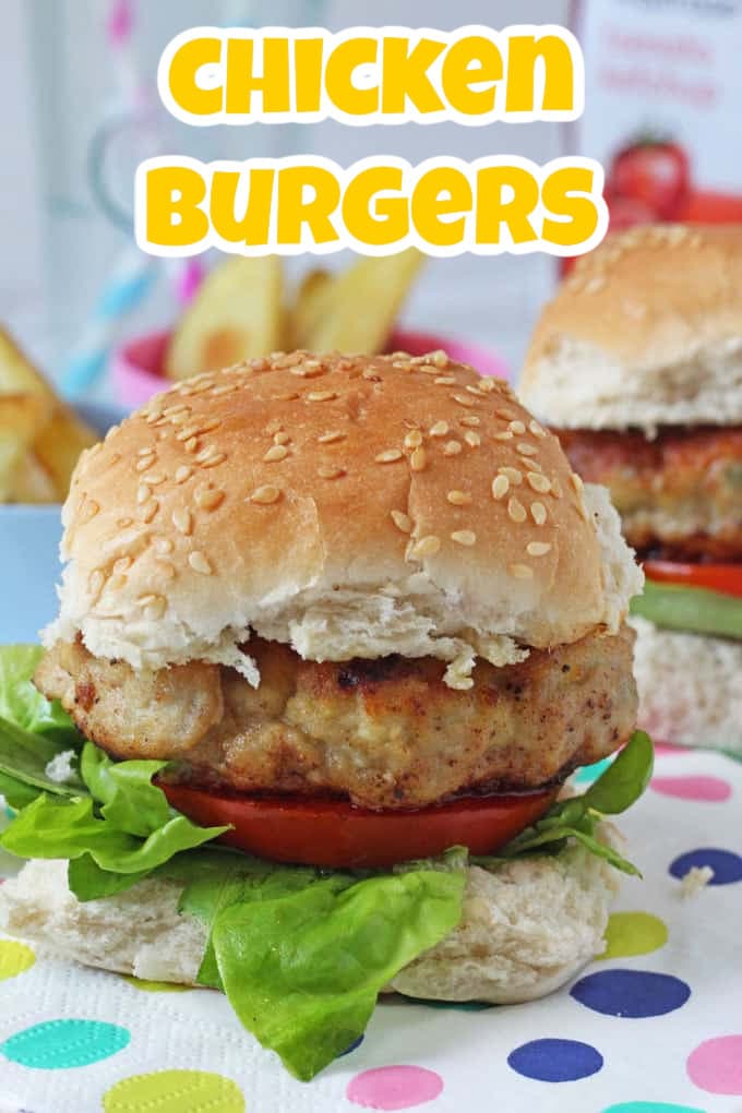 A chicken burger in a seeded bun with slices of tomato and lettuce leaves.