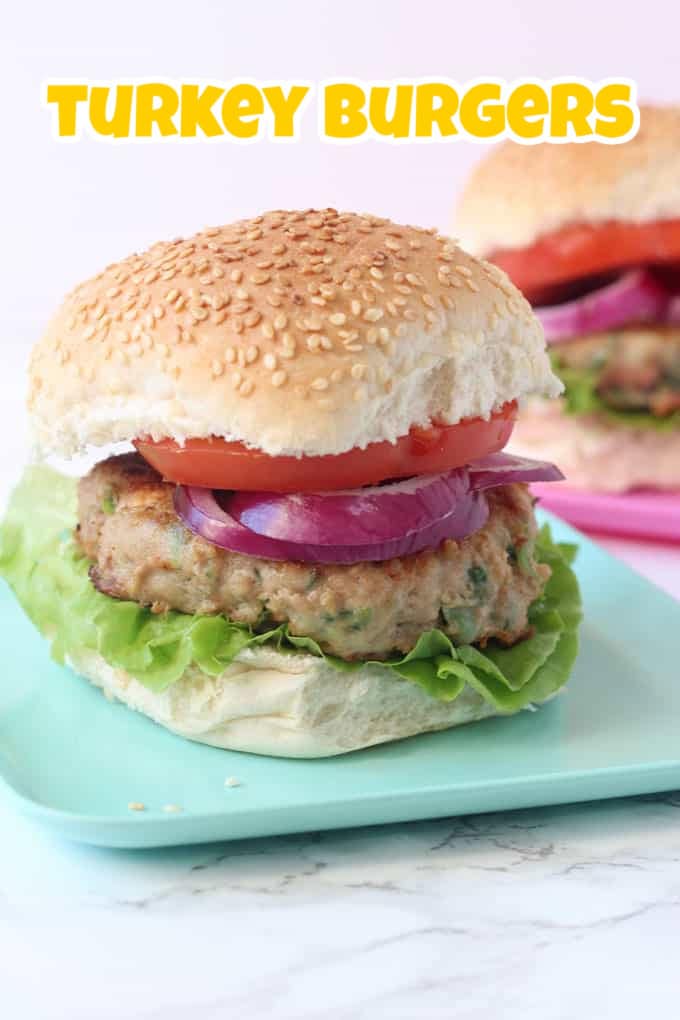 A turkley burger in a seeded bun with lettuce leaves,  and sliced tomato and onions.