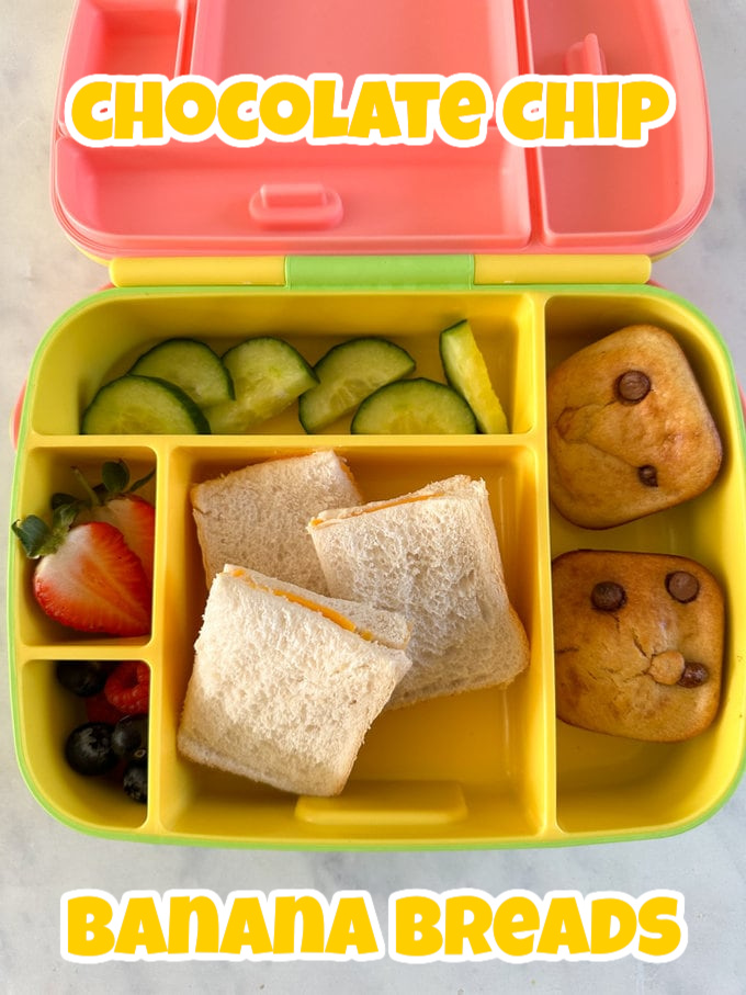 2 Mini Chocolate Chip Banana breads in a yellow compartment lunchbox with a cheese sandwich and fresh chopped fruits and cucumber.