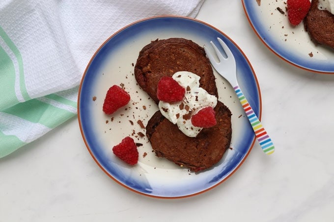 Easy Make-Ahead Breakfast Recipes & Ideas For Kids - Two plates of chocolate raspberry pancakes topped with a dollop of greek yogurt and fresh raspberries