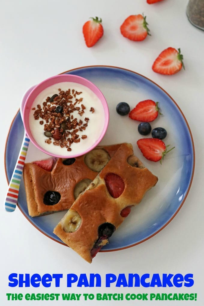 2 Slices of sheet pan pancake on a blue plate with a small pot of yogurt and granola and a few fresh berries on the side.