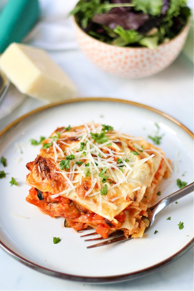 A slice of Chicken Lasagne served on a white plate, garnished with fresh herbs and grated parmesan