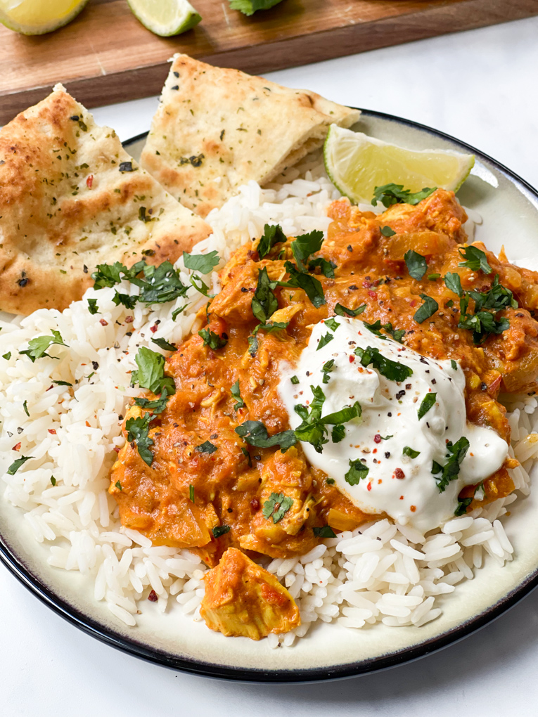 a close up shot of the slow cooker chicken tikka masala served on the plate with all the sides and garnishes.