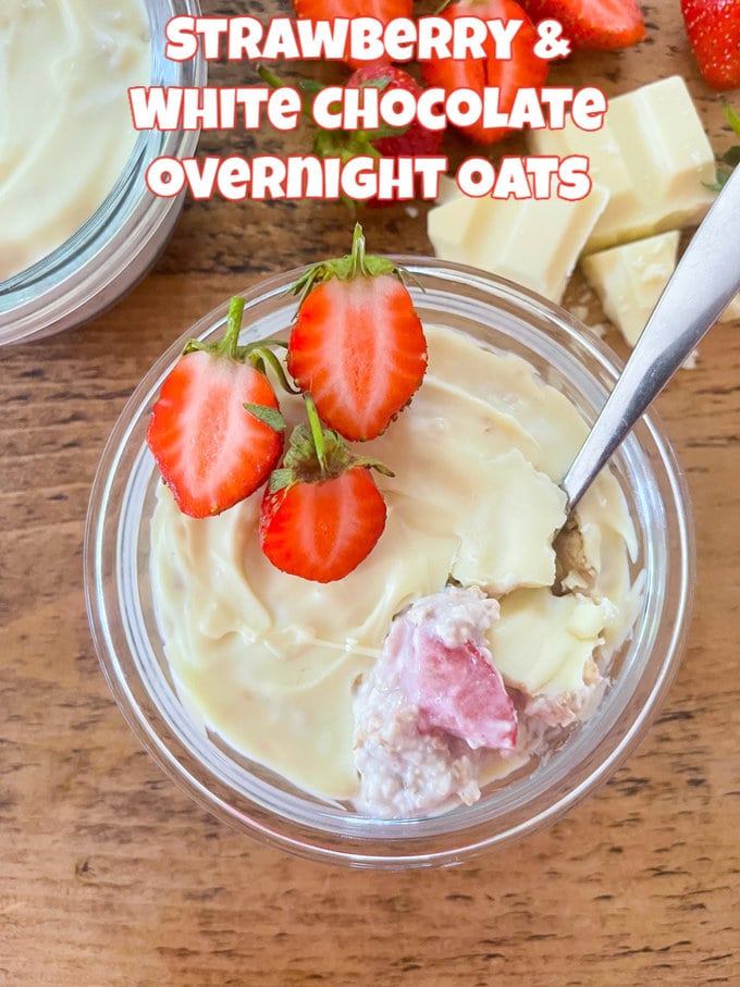 Strawberry & White chocolate overnight oats in a glass ramekin topped with fresh chopped strawberries and a teaspoon.
