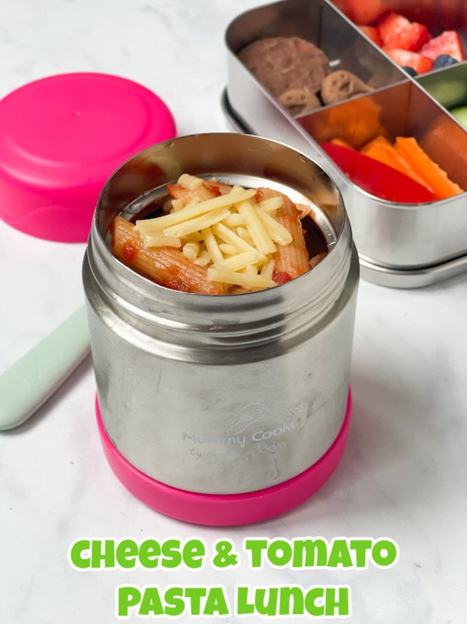 Cheese and tomato pasta topped with grated cheddar cheese served in a metal food flask with a bright pink lid.
