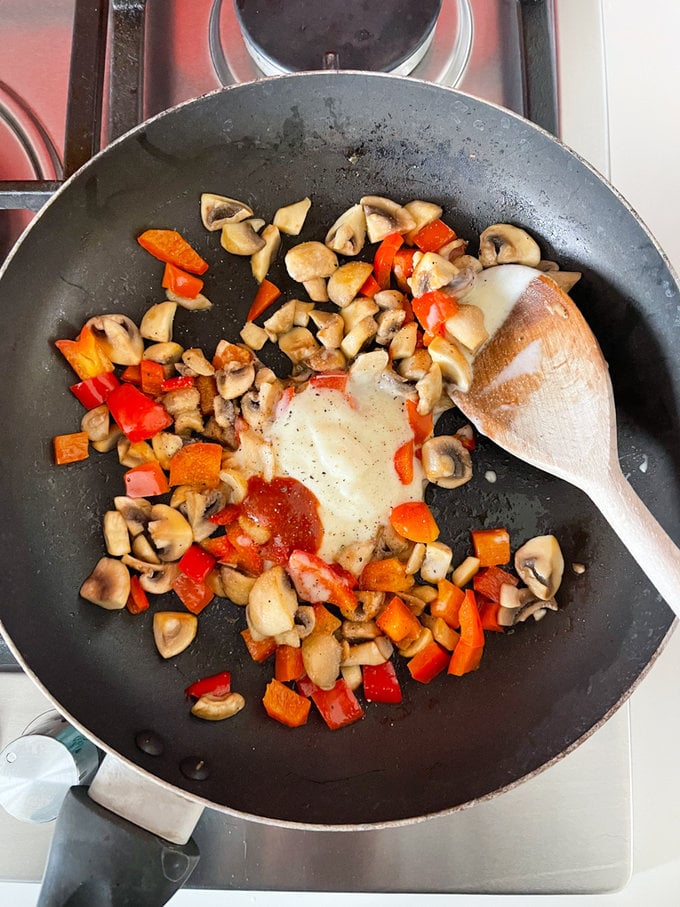 Cheese spread and chilli sauce being added to the cooked peppers and mushrooms.