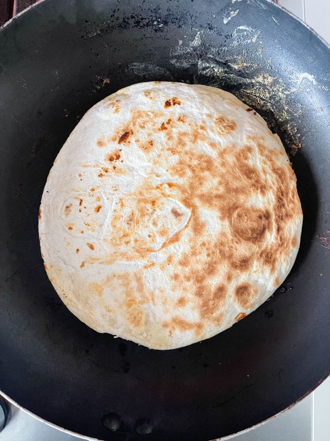 Another wrap is placed on top to create a sandwich in the frying pan.