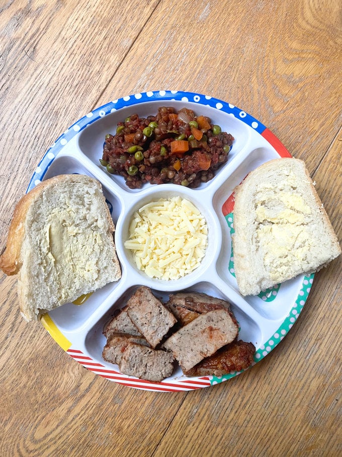 Sausage casserole served on a divided plate for kids with a side serving of buttered crusty bread.
