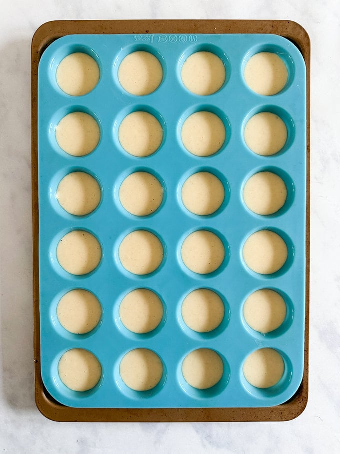 Pancake batter being poured into a blue silicone muffin tray.