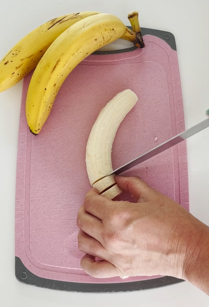 Bananas being chopped into slices on a pink chopping board.