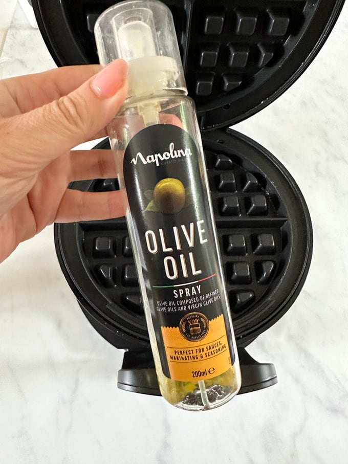 Olive oil being sprayed onto the surface of the waffle maker.