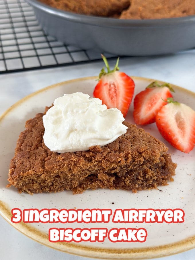 A slice of Airfryer Biscoff Cake on an off white plate, topped with chopped strawberries and a dollop of greek yogurt on top.