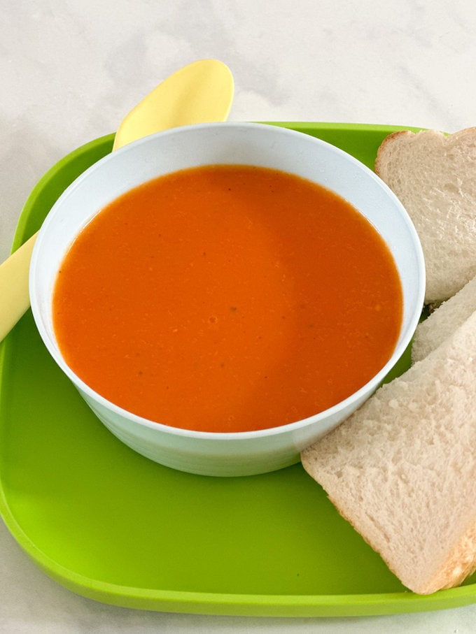 Roasted tomato and red pepper soup served in a white bowl with bread on the side.