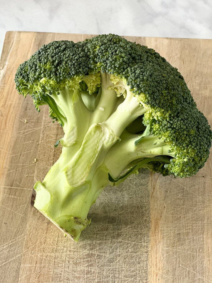 A head of broccoli laying on a wooden chopping board.