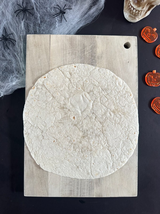 Plain tortilla wrap laying on a wooden chopping board.