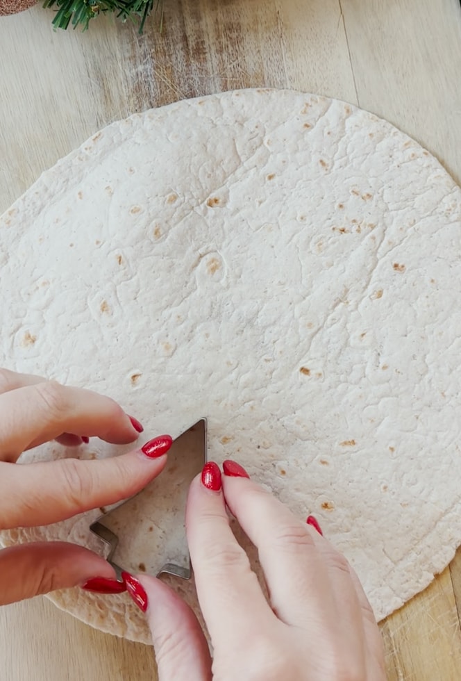 Christmas tree shapes being cut of the tortilla wrap using a shaped pastry cutter.