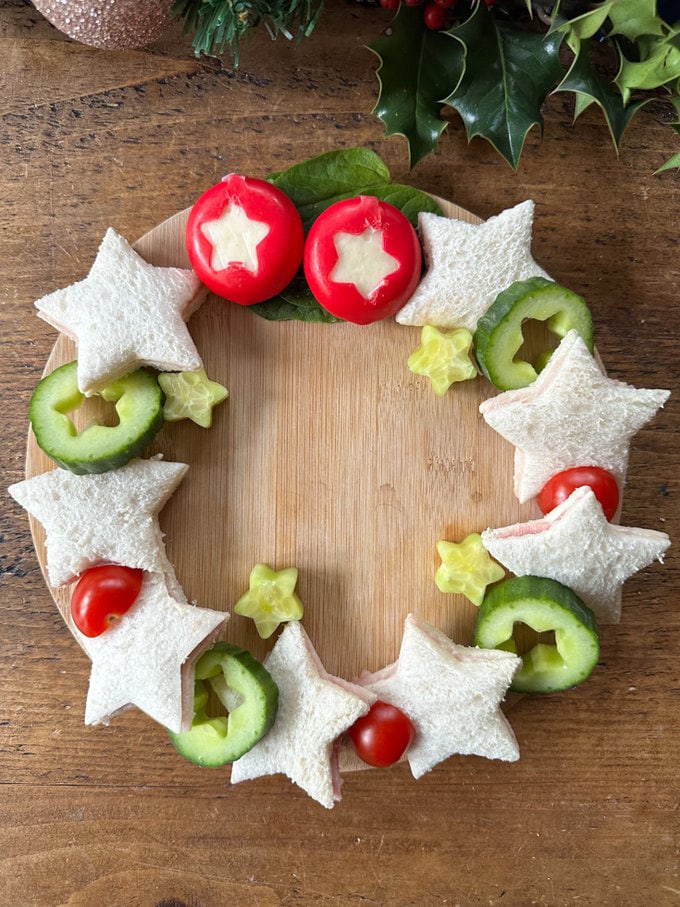 Christmas Sandwich Wreath arranged on a round wooden chopping baord.