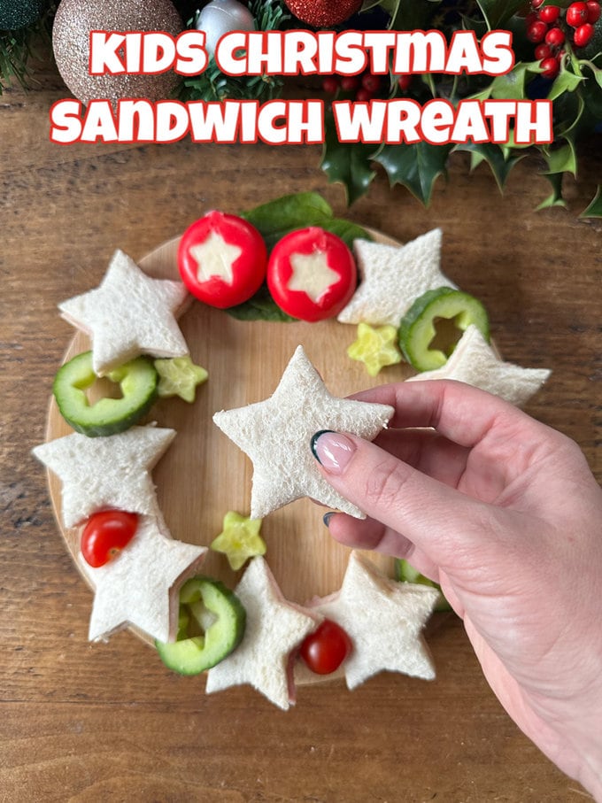 Kids Christmas Sandwich Wreath served on a wooden board with mini cheeses and cucumber with stars cut out of them.