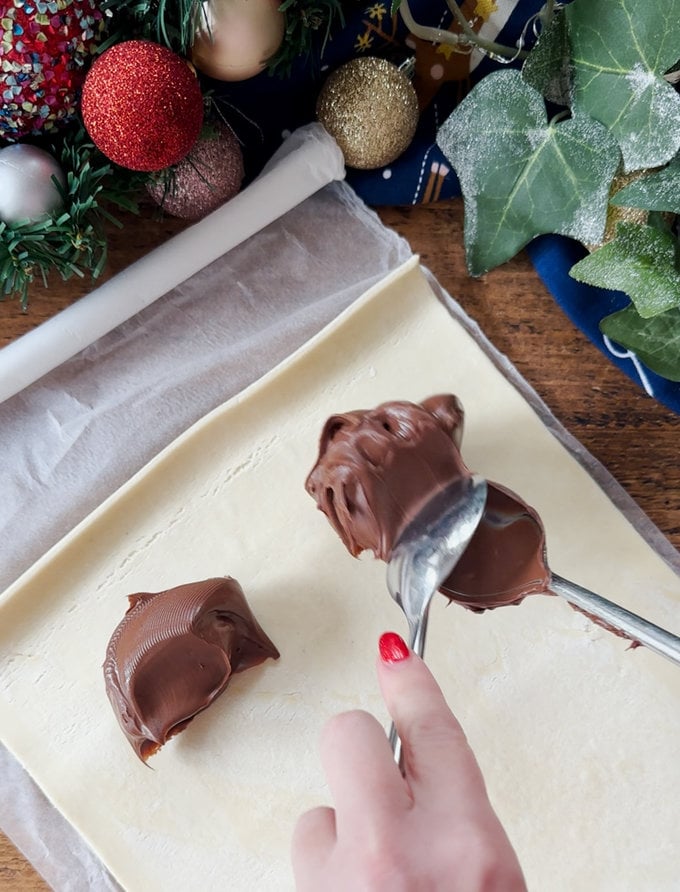 Nutella being spread into the raw puff pastry with two spoons.