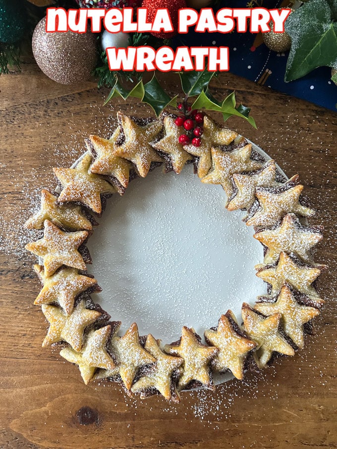 Nutella Pastry Wreath dusted with icing sugar on a white plate with Christmas decorations in the background.