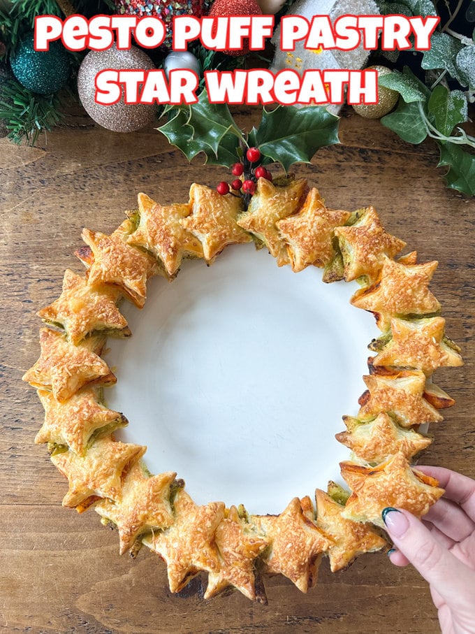 Pesto Puff Pastry Star Wreath on a white plate with holly and Christmas decorations in the background.