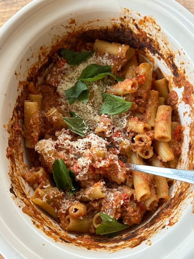 the cooked sausage ragu in the slow cooker garnished with fresh basil leaves and finely grated parmesan.