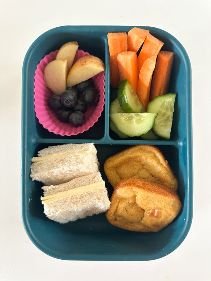 Mini Carrot Banana Bread served in a divided lunch box along with a sandwich and fresh berries and cucumber.