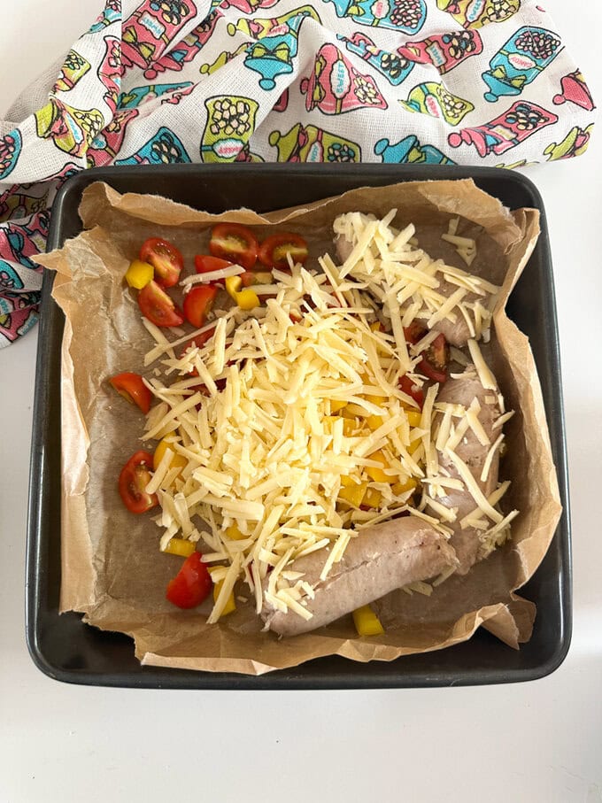 Lined oven dish with parchment paper and add in 3 sausages (with skins removed), cherry tomatoes, yellow pepper and grated cheese.