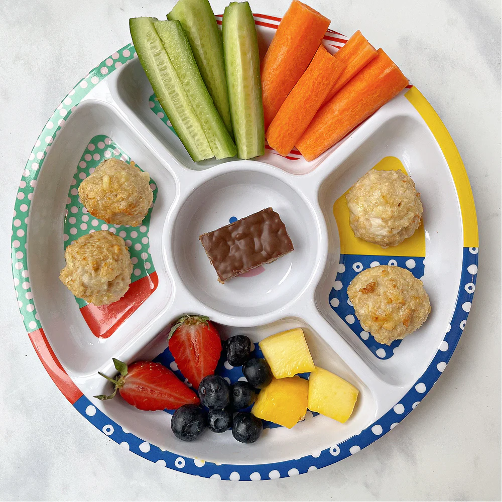 Cheesy Chicken Meatballs served in a colourful divided kids plate from Pick Plates with chopped veggies, fruit and a chocolate flapjack.