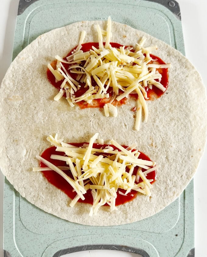 Pizza toaster wrap being assembled, being topped with passata and grated cheese.