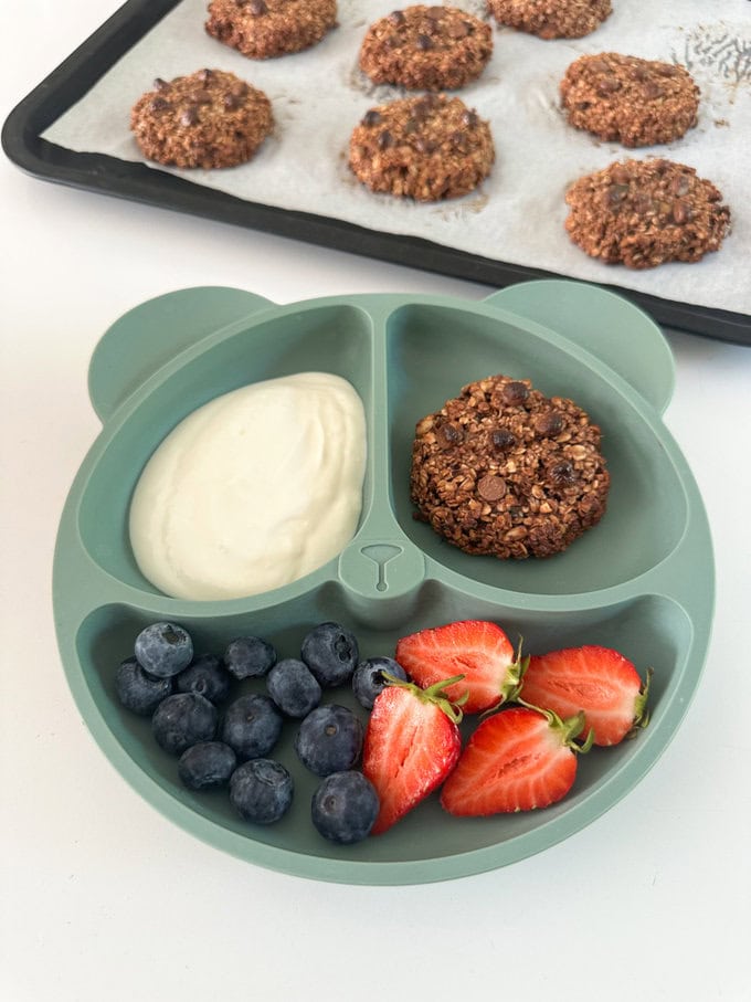 Nutella Breakfast Cookies served on a divided children's plate with a dollop of yogurt and fresh chopped fruit.