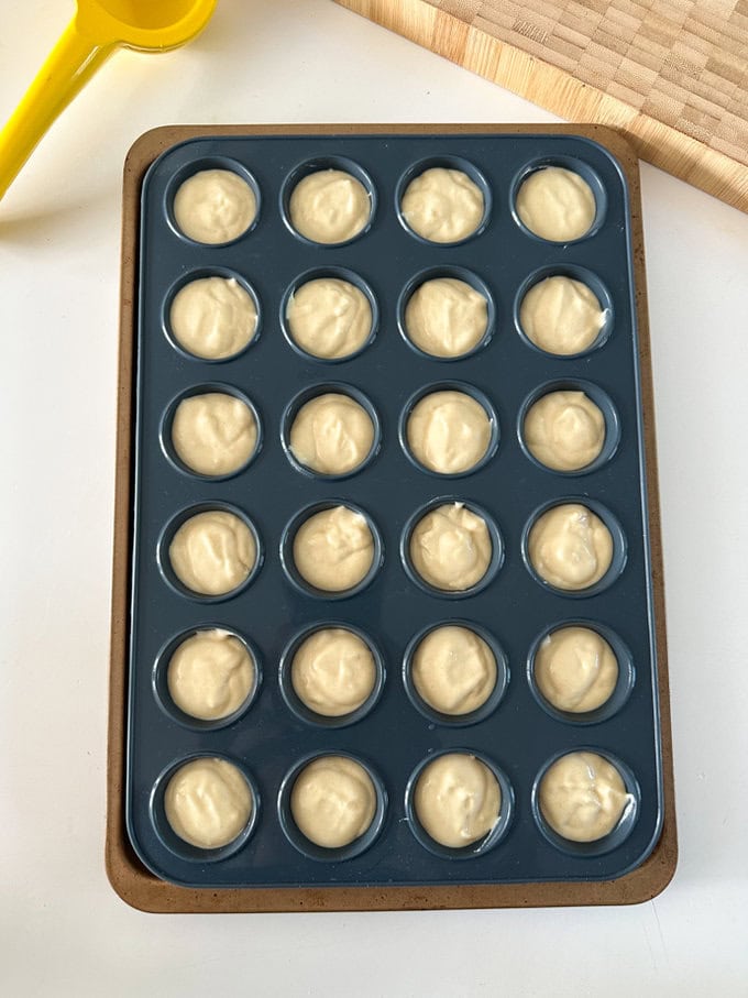 Mini lemon muffin batter mix being added to a silicone mini muffin tray, ready for the oven.