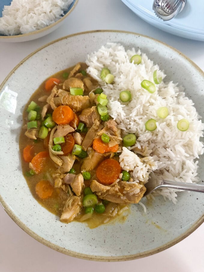 Slow Cooker Mayflower Chicken Curry served on a round white dinner plate, served with white fluffy rice and garnished with chopped spring onions.