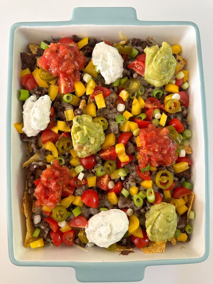 Easy nachos served in a large sharing dish and garnished with peppers,spring onions and cherry tomatoes. with dollops sour cream and guacamole.