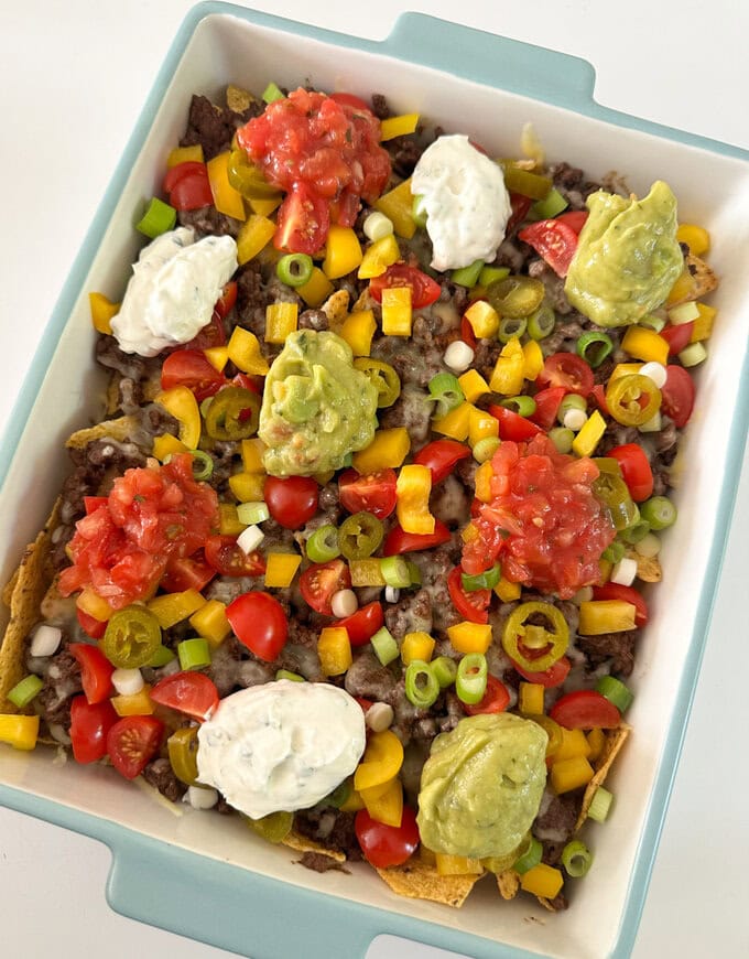 Easy nachos served in a large sharing dish and garnished with peppers,spring onions and cherry tomatoes. with dollops sour cream and guacamole.