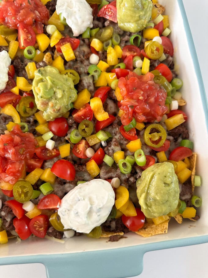 Easy nachos served in a large sharing dish and garnished with peppers,spring onions and cherry tomatoes. with dollops sour cream and guacamole.
