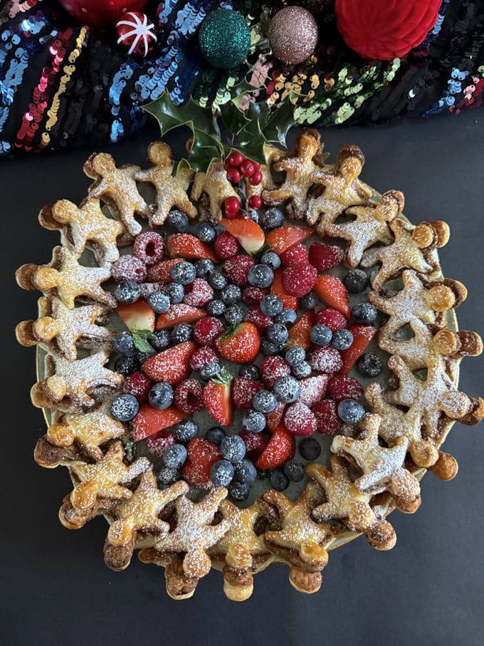Gingerbread man puff pastry wreath presented with fresh berries and dusted in icing sugar.