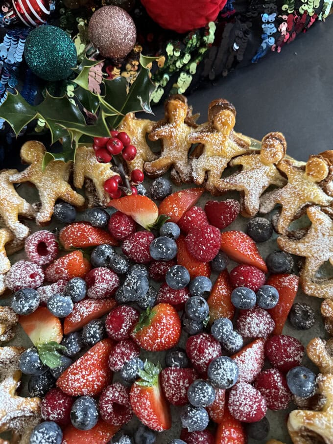 Gingerbread man puff pastry wreath presented with fresh berries and dusted in icing sugar.