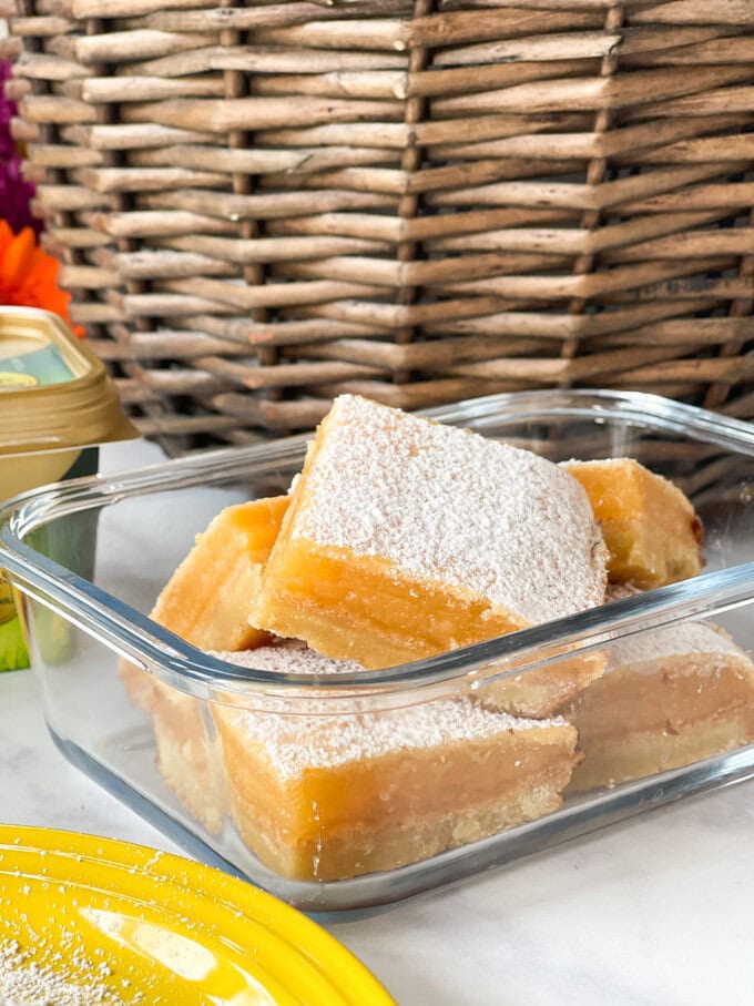 Lemon bars in a clear glass Tupperware container.