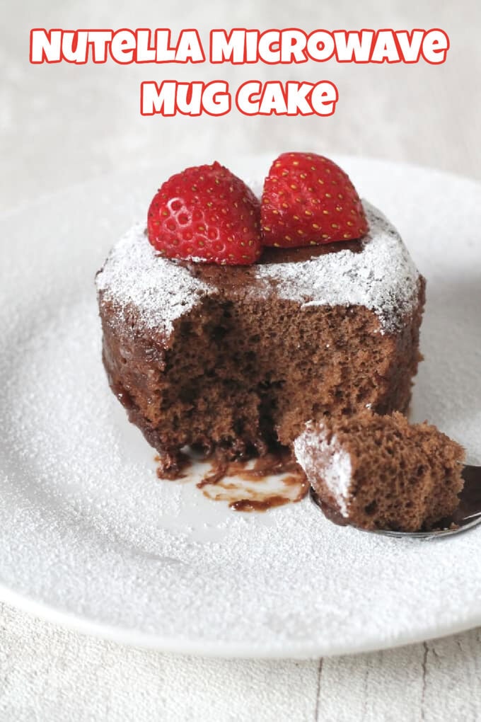 An individual Nutella Microwave Mug Cake served on a white plate with two strawberry halves on top and dusted with icing sugar.