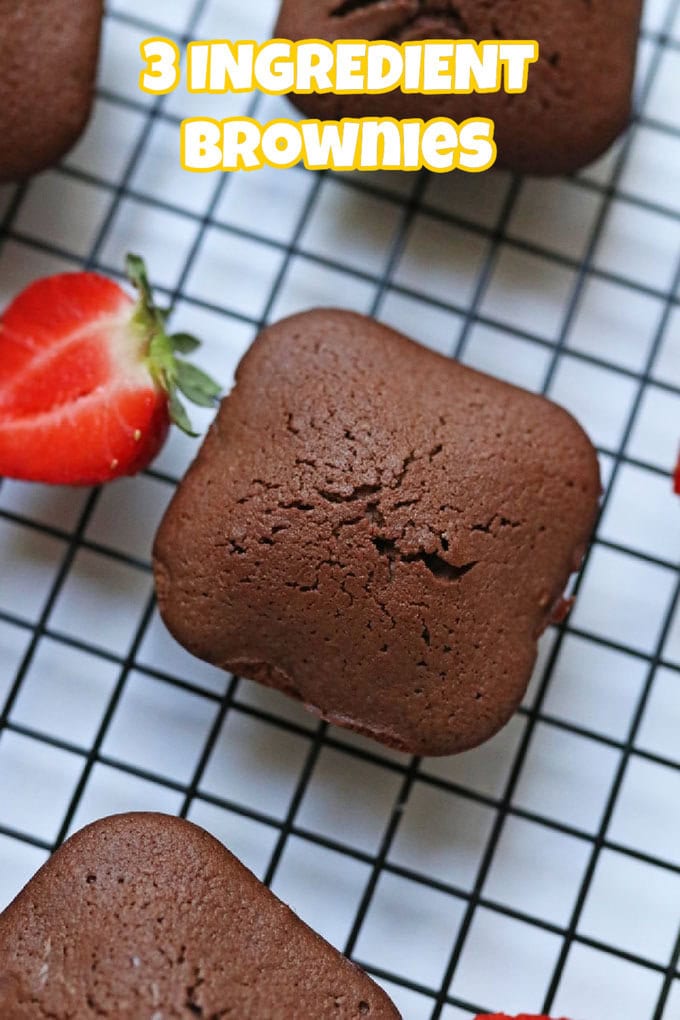 A closeup of one of the three ingredient brownies on a black wire cooling rack with half a chopped strawberry next to it.