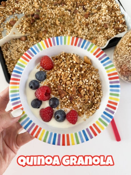 Quinoa Granola served in a multicolored striped bowl with yogurt and fresh raspberries and blueberries.