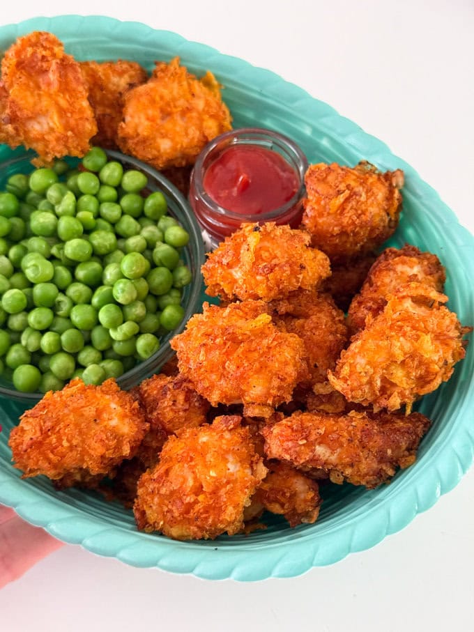 Crispy Cornflake Chicken Nuggets served in a blue basket style bowl along with a small bowl of garden peas and tomato ketchup for dipping.