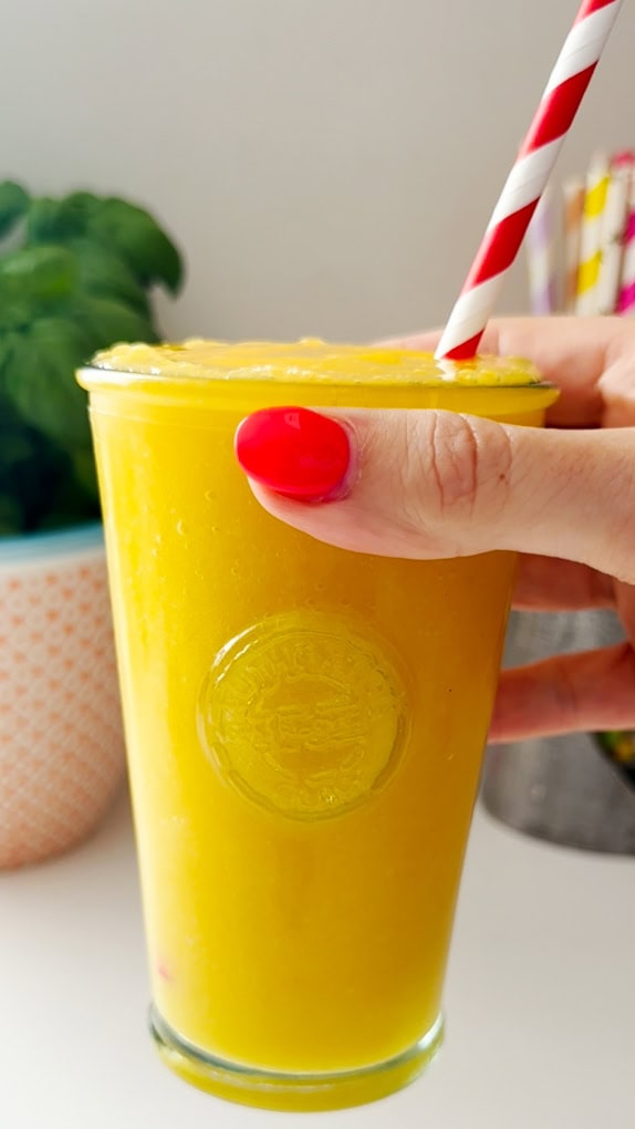 Mango & Passion Fruit Cooler served in a tall clear glass with a red and white stripy straw in the drink.