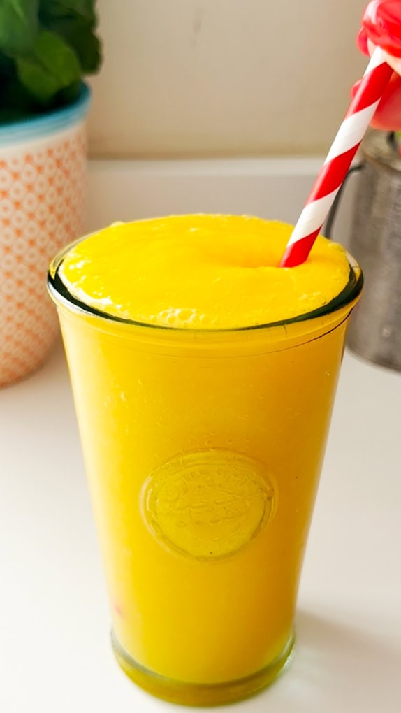 Mango & Passion Fruit Cooler served in a tall clear glass with a red and white stripy straw in the drink.