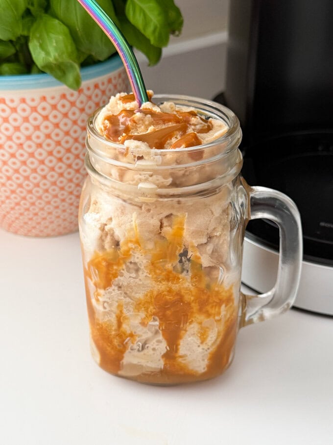 Ninja Creami Coffee Frappe served in a Milkshake glass drizzled with caramel sauce and a straw popped in the top.